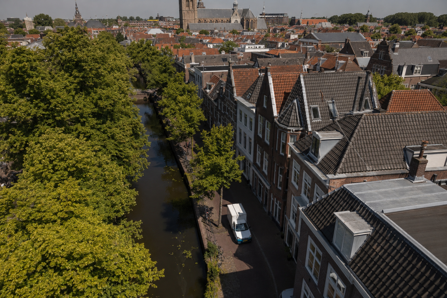 Luchtfoto van de Delftse binnenstad met grachten en een elektrische bestelauto op een smal straatje